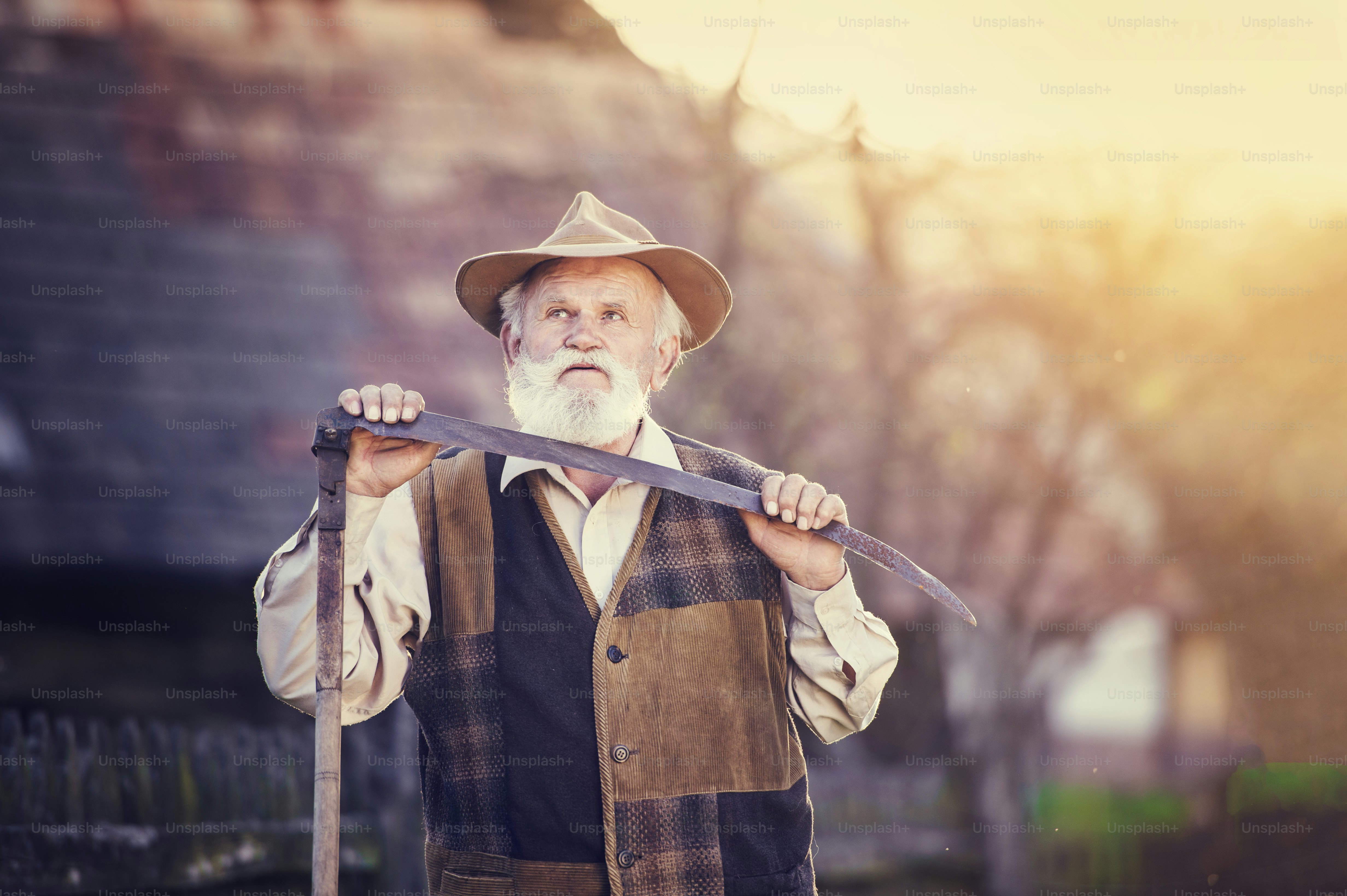 Old farmer with scythe taking a break from mowing the grass