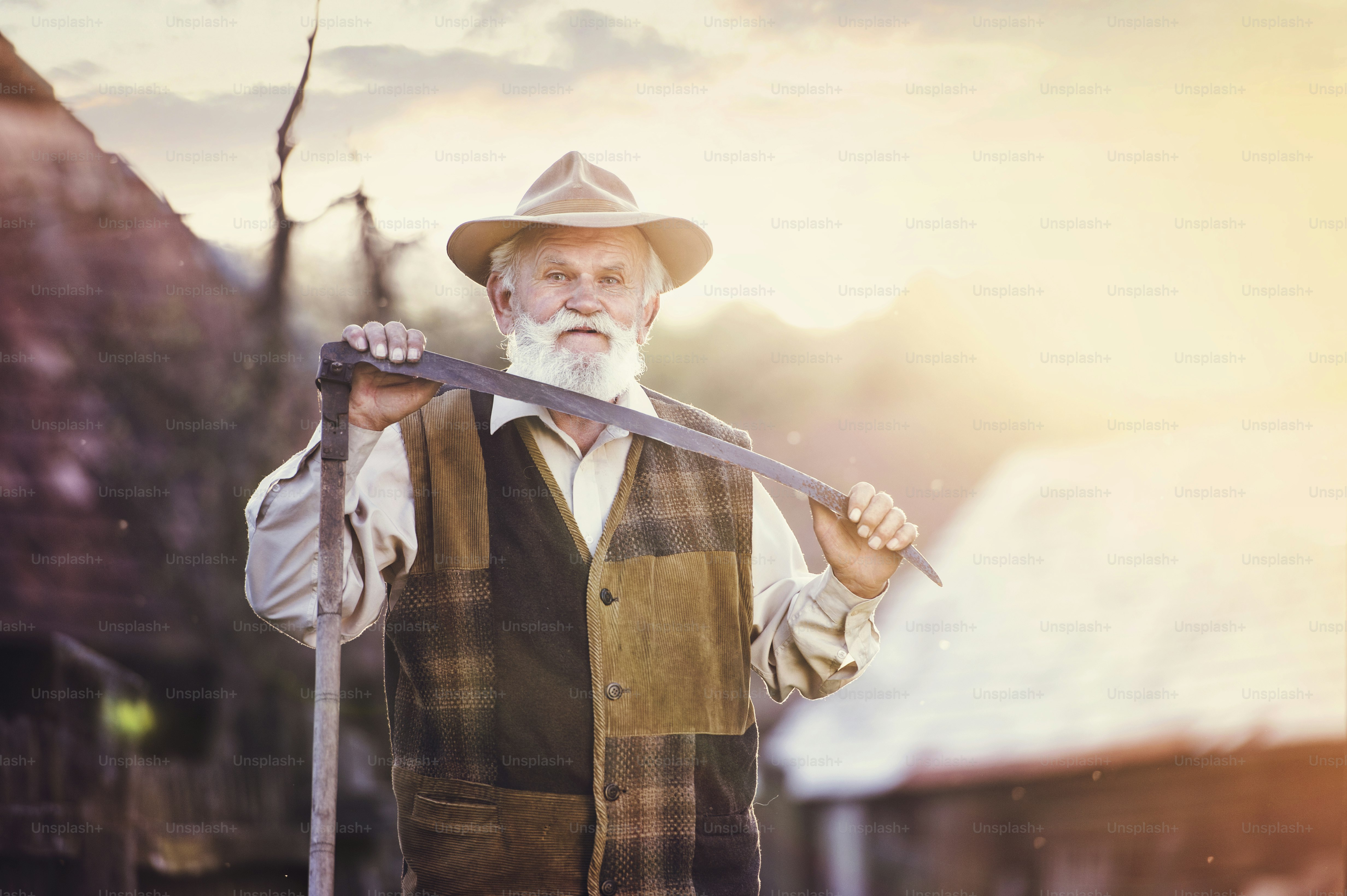 Old farmer with scythe taking a break from mowing the grass