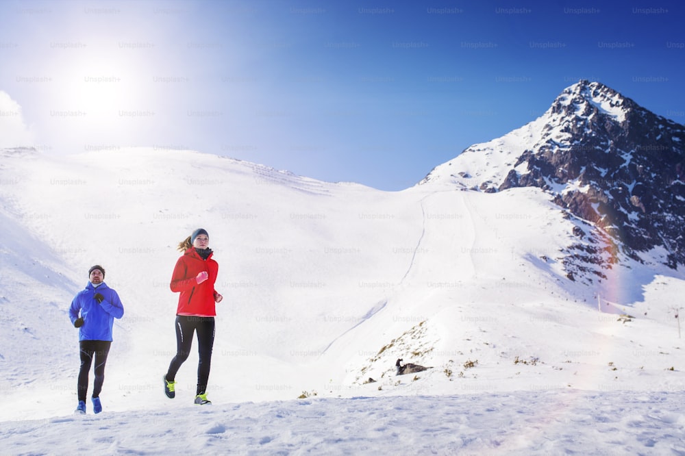 Jeune couple faisant du jogging à l’extérieur dans les montagnes ensoleillées d’hiver