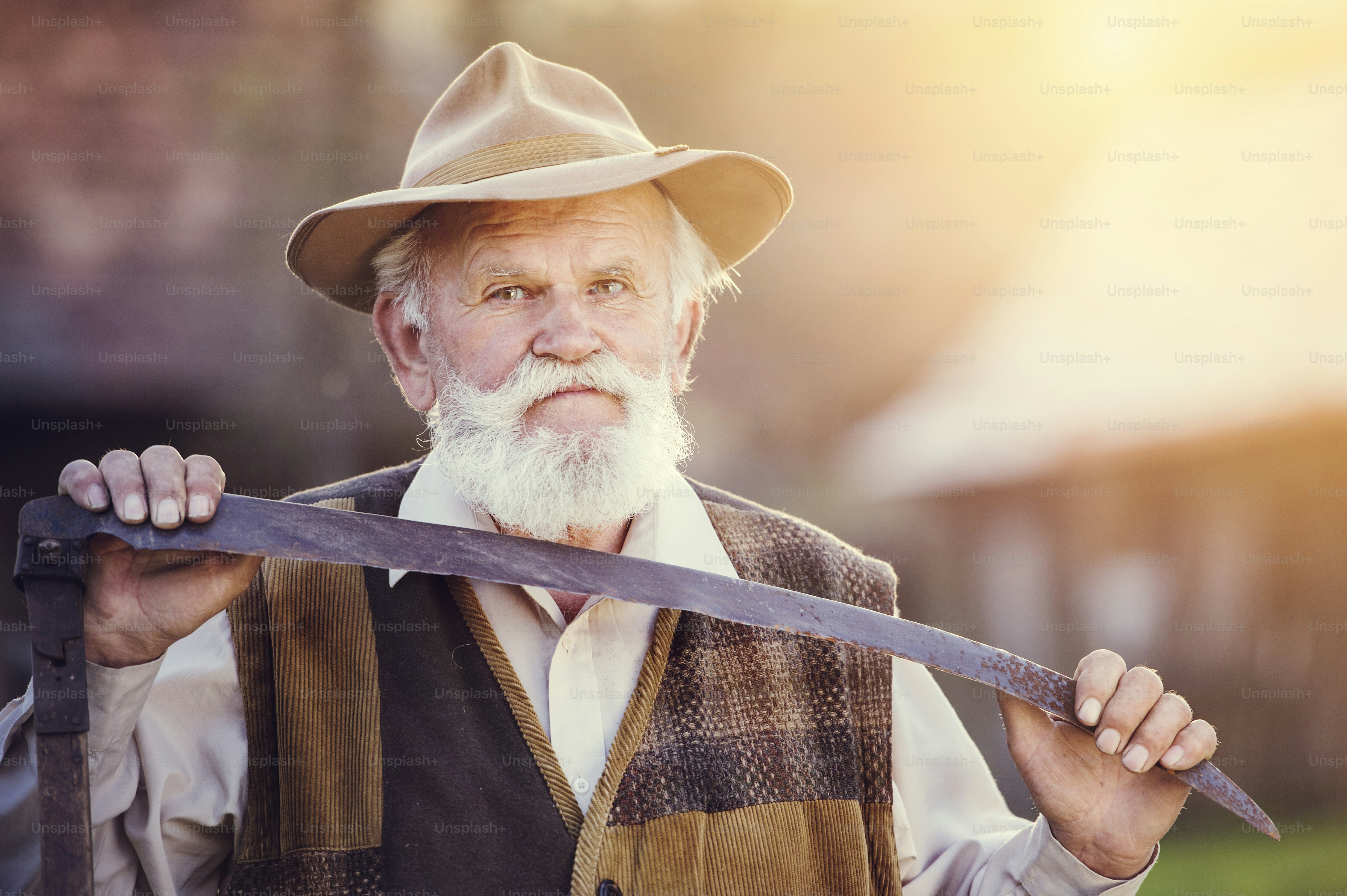Old farmer with scythe taking a break from mowing the grass