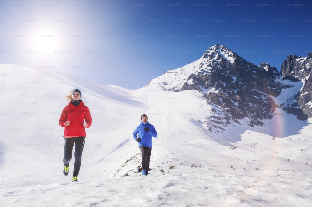 Casal jovem correndo ao ar livre em montanhas ensolaradas de inverno