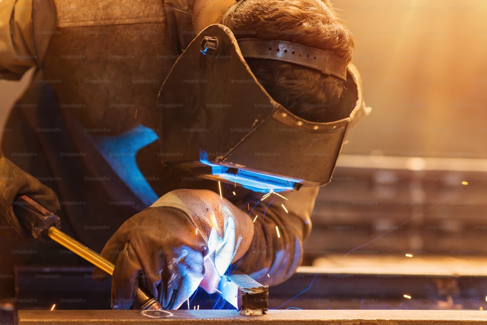 Young man with protective mask welding in a factory