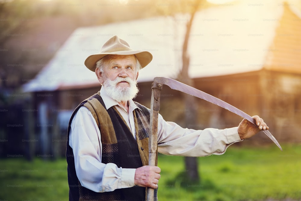 Old farmer with scythe taking a break from mowing the grass