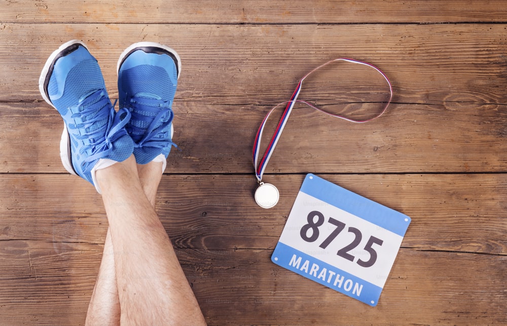 Legs of a runner, medal and race number on a wooden floor background