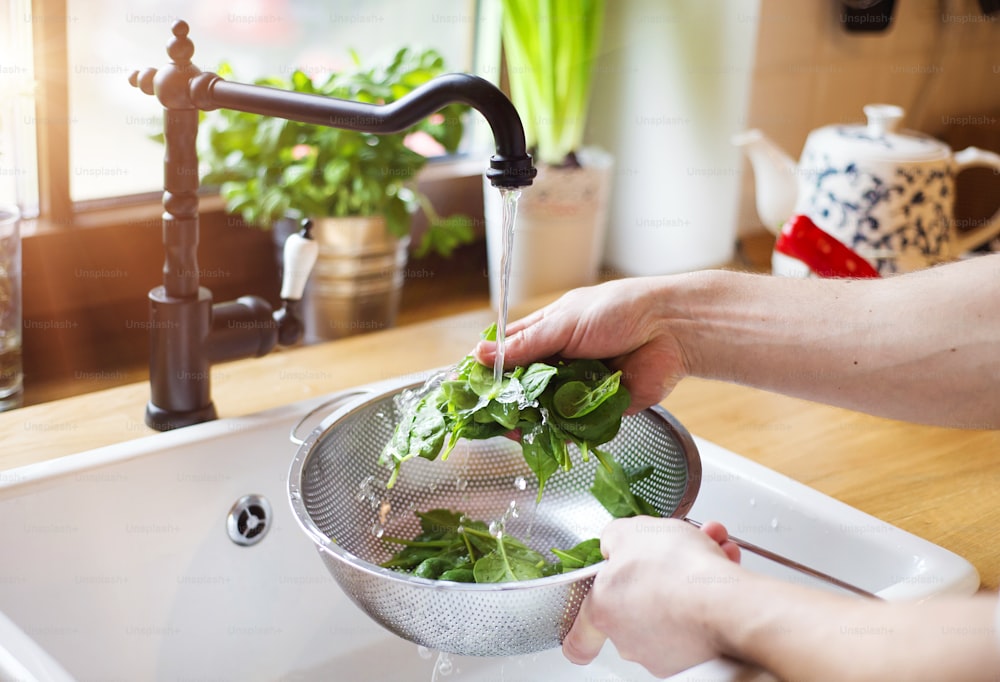 Hombre irreconocible lavando hojas verdes de ensalada en el fregadero de la cocina