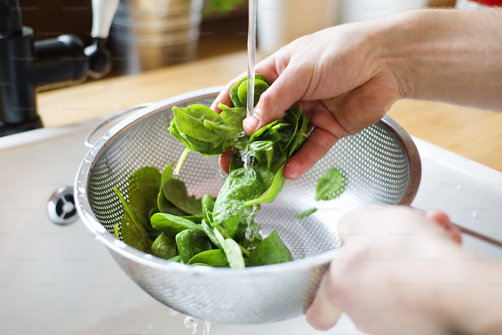 Uomo irriconoscibile che lava le foglie di insalata verde nel lavandino della cucina