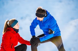 Young man having a knee injury while jogging outside in sunny winter mountains