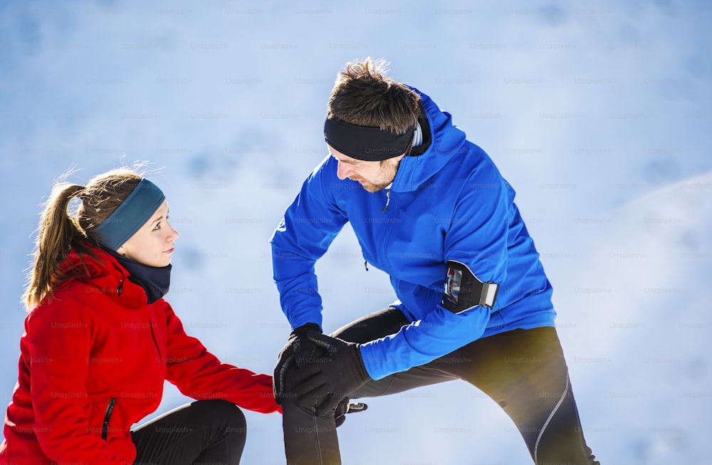 Young man having a knee injury while jogging outside in sunny winter mountains
