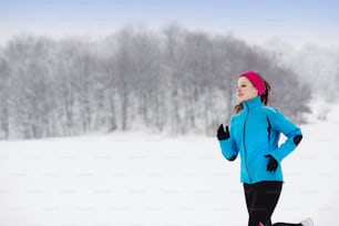 Athlete woman is running during winter training outside in cold snow weather.