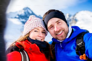 Young couple taking selfie on a hike outside in sunny winter mountains