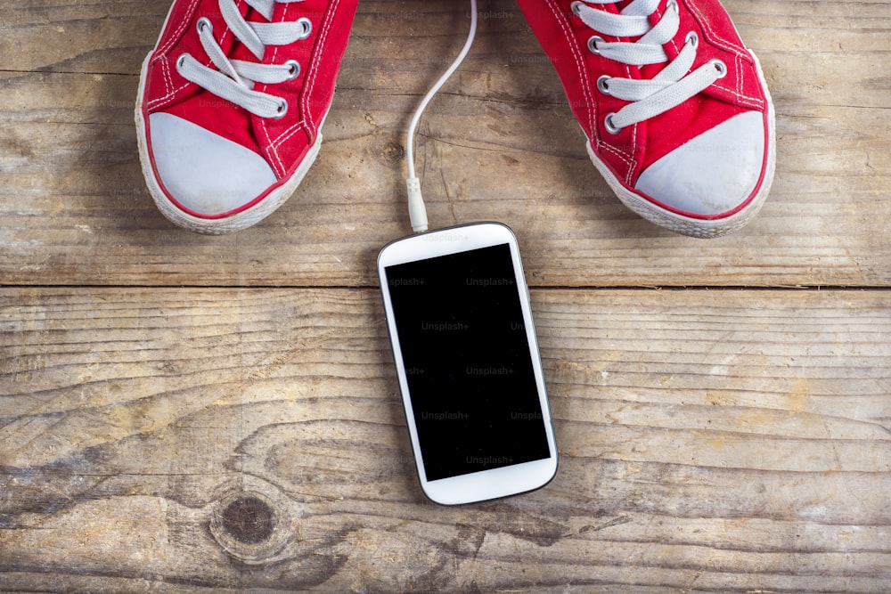 Concept with red sneakers and tablet with white headphones laid on wooden floor background.