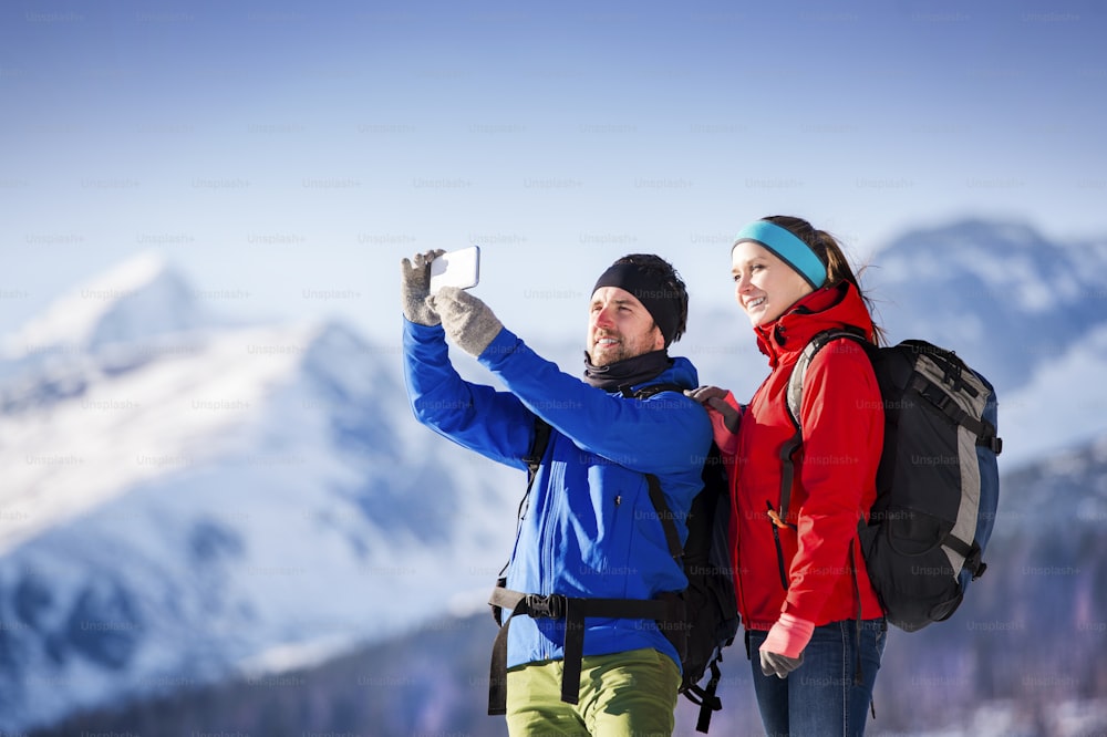 Young couple taking selfie on a hike outside in sunny winter mountains