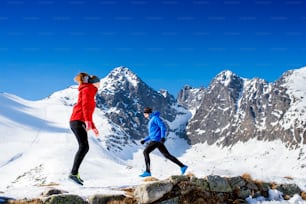 Young couple warming up before jogging outside in sunny winter mountains