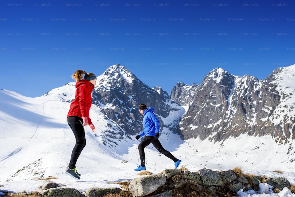 Young couple warming up before jogging outside in sunny winter mountains