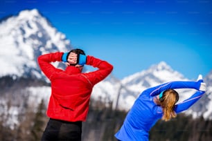 Young couple stretching before jogging outside in sunny winter mountains