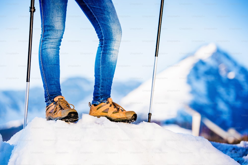 Unkenntliche Frau, die draußen in sonnigen Winterbergen wandert