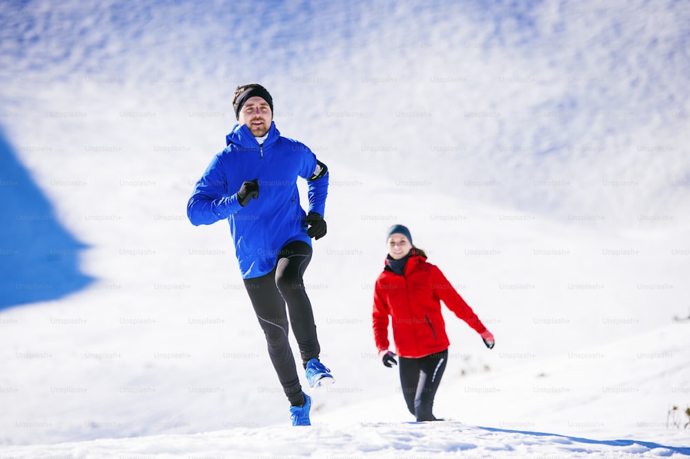 Junges Paar joggt draußen in sonnigen Winterbergen