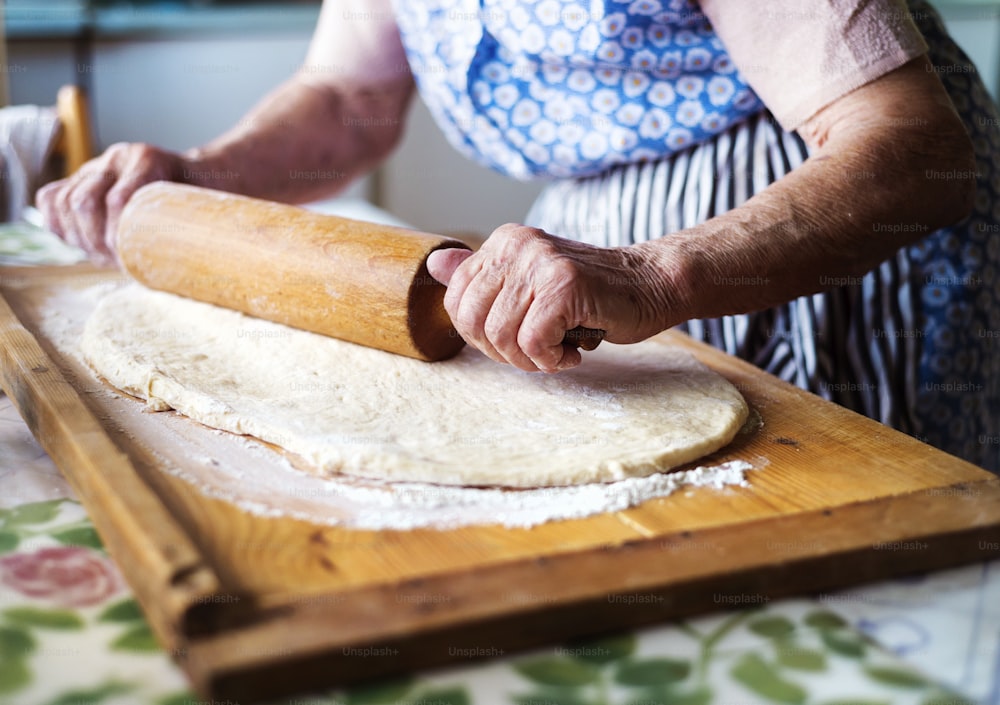 Senior woman baking pies in her home kitchen. Rolling dough using rolling pin.