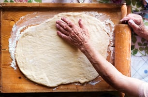 Une femme âgée fait des tartes dans sa cuisine à la maison. Rouler la pâte à l’aide d’un rouleau à pâtisserie.