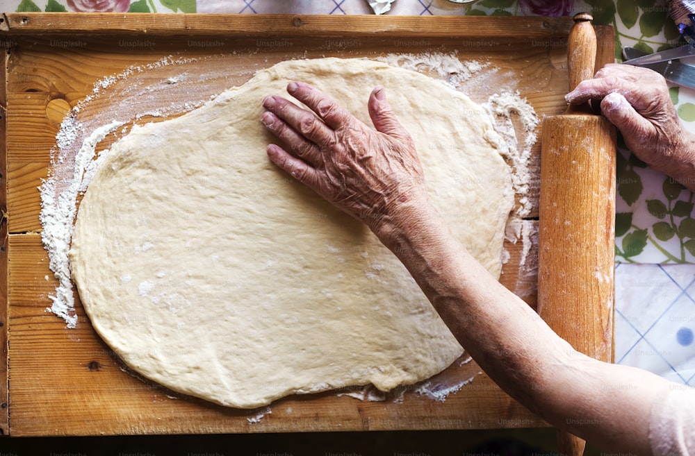 Senior woman baking pies in her home kitchen. Rolling dough using rolling pin.