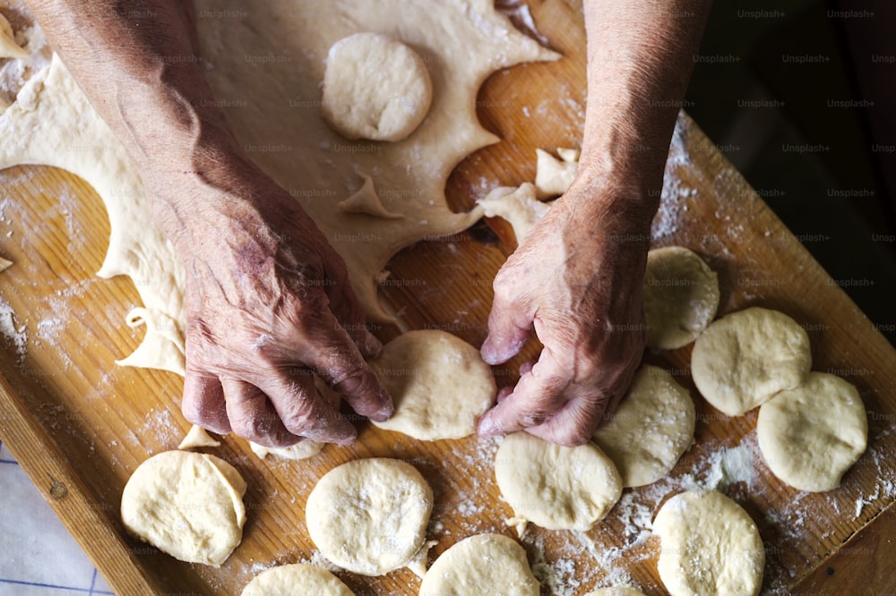 Mujer mayor horneando pasteles en la cocina de su casa. Cortar círculos de masa cruda.