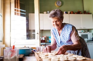 Ältere Frau backt Kuchen in ihrer heimischen Küche. Kreise aus rohem Teig ausschneiden.