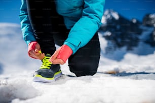 Young runner tying her shoelaces outside in winter nature