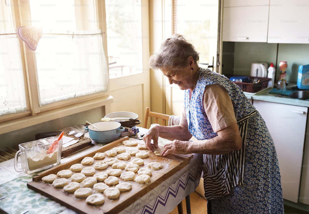 Une femme âgée fait des tartes dans sa cuisine à la maison. Découper des cercles dans la pâte crue.