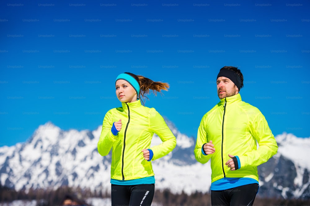 Young couple jogging outside in sunny winter mountains