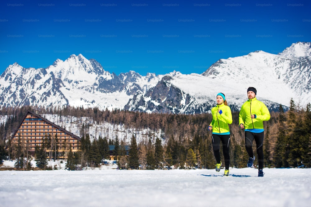Giovane coppia che fa jogging fuori nelle montagne soleggiate di inverno