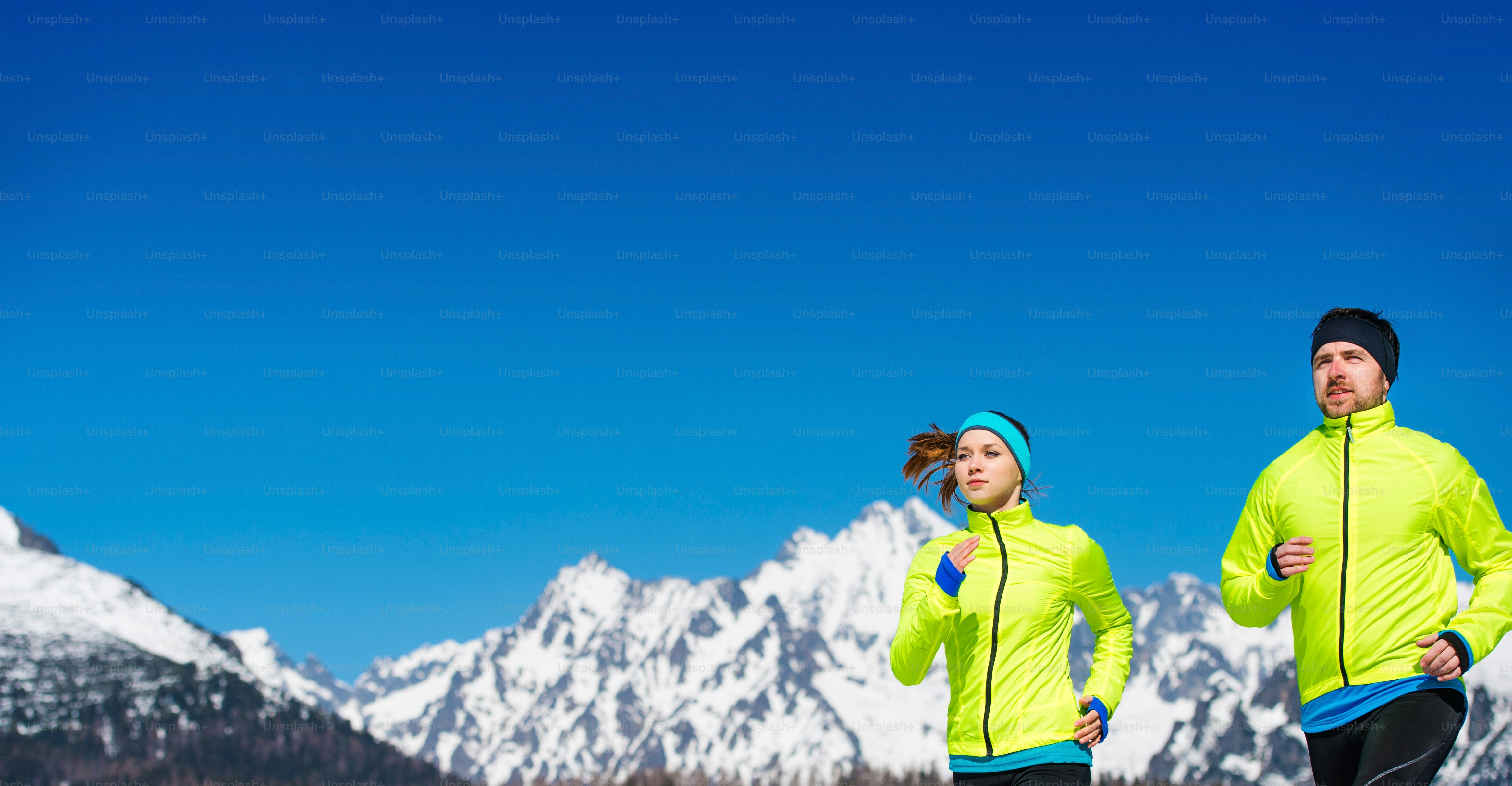 Young couple jogging outside in sunny winter mountains