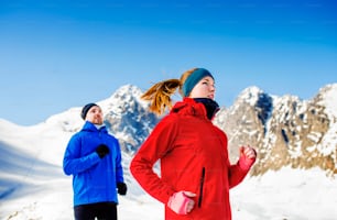 Young couple jogging outside in sunny winter mountains