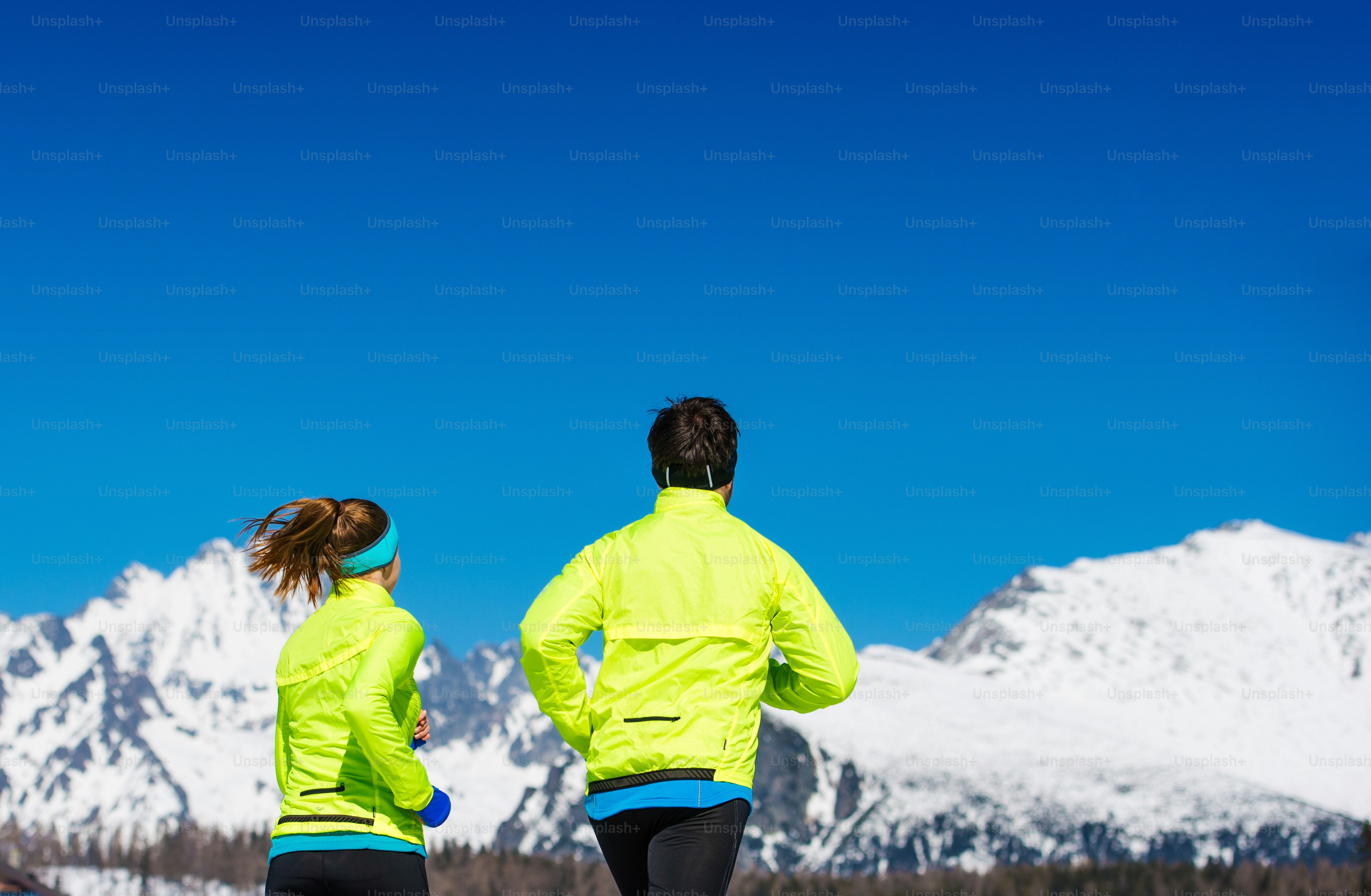 Young couple jogging outside in sunny winter mountains