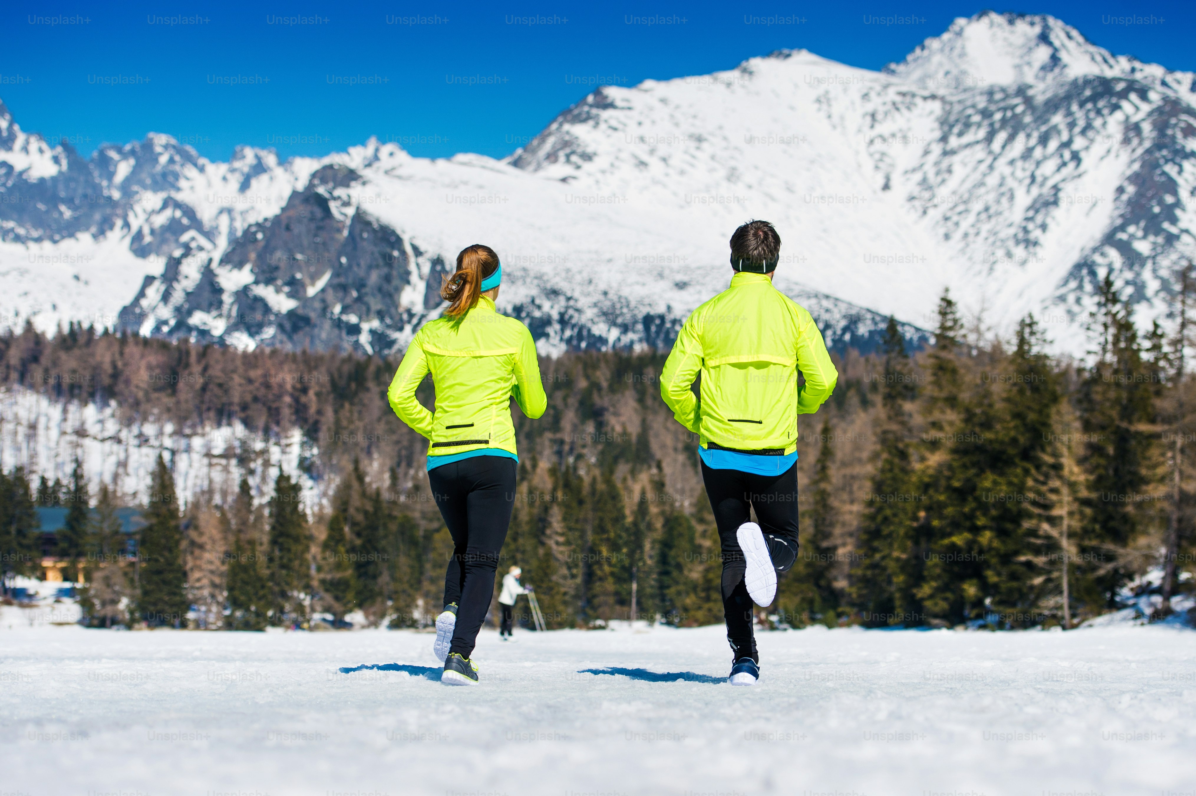 Young couple jogging outside in sunny winter mountains