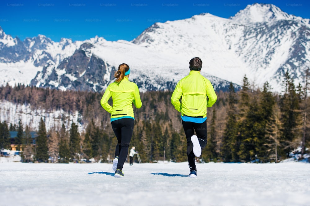 太陽の光が降り注ぐ冬の山々で外をジョギングする若いカップル