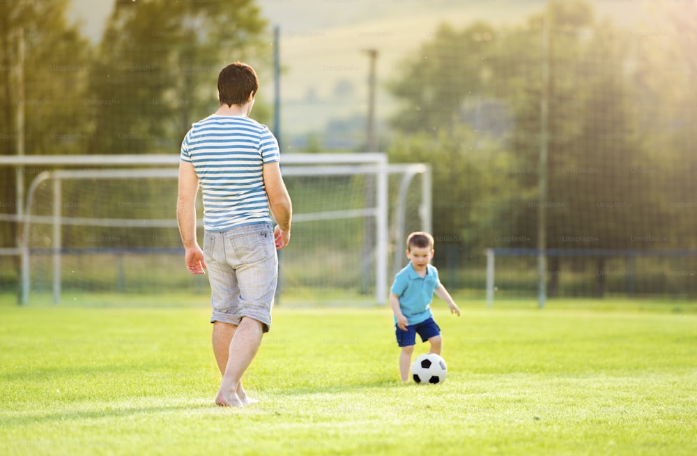 Junger Vater mit seinem kleinen Sohn beim Fußballspielen auf dem Fußballplatz