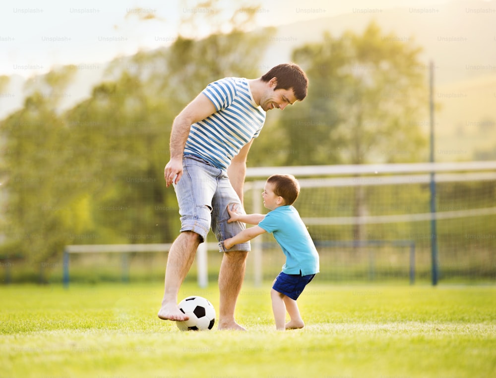 Pai jovem com seu filho pequeno jogando futebol no campo de futebol