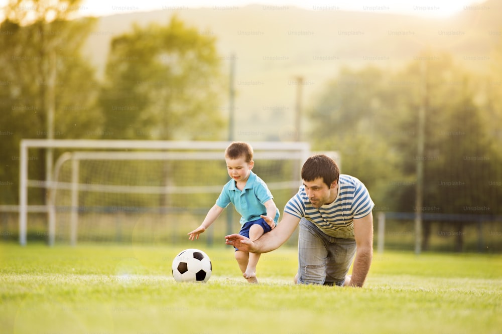 サッカー場でサッカーをしている幼い息子と若い父親