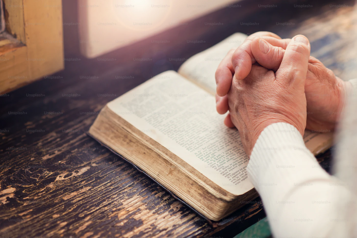 Folded hands in prayer resting on an open Bible