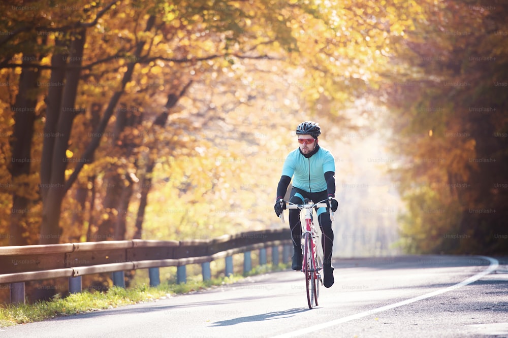 Giovane sportivo bello in sella alla sua bicicletta all'aperto nella natura soleggiata di autunno