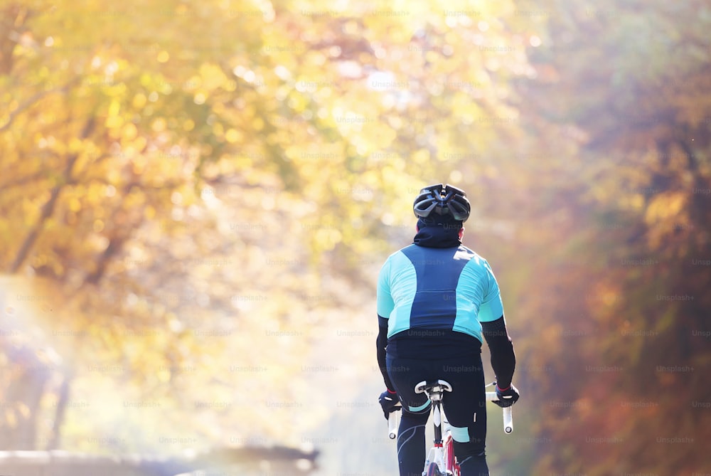 Giovane sportivo bello in sella alla sua bicicletta all'aperto nella natura soleggiata di autunno