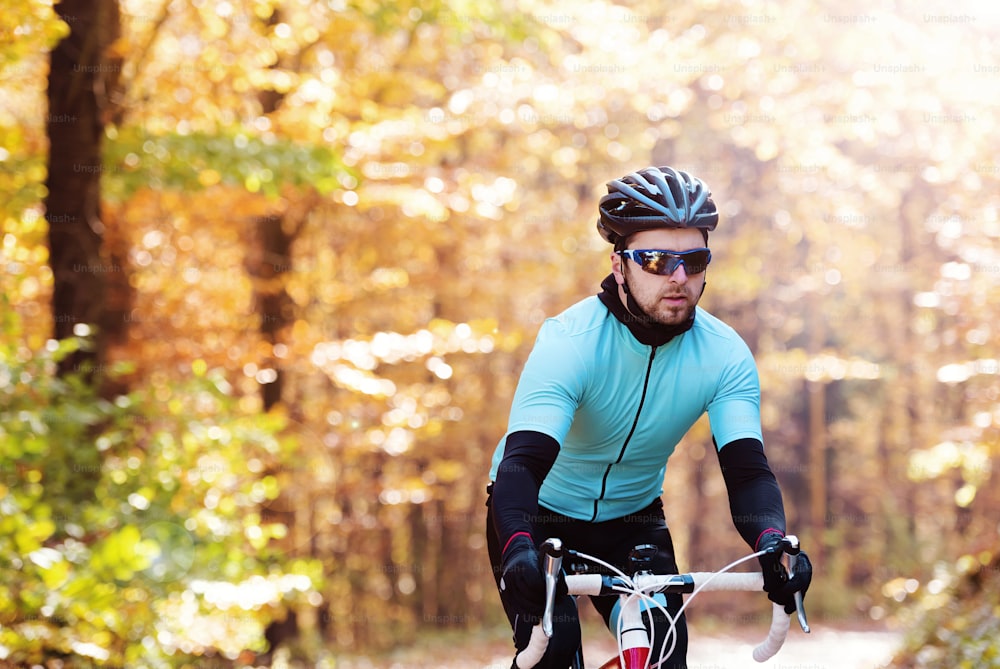 Giovane sportivo bello in sella alla sua bicicletta all'aperto nella natura soleggiata di autunno