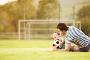 Jeune père avec son petit garçon jouant au football sur un terrain de football