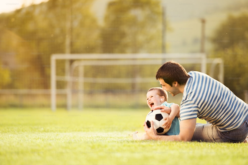 Young father with his little son playing football on football pitch