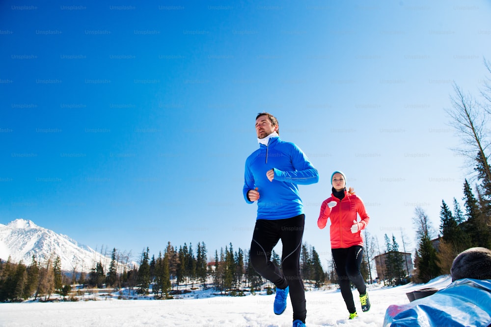 Young couple jogging outside in sunny winter mountains