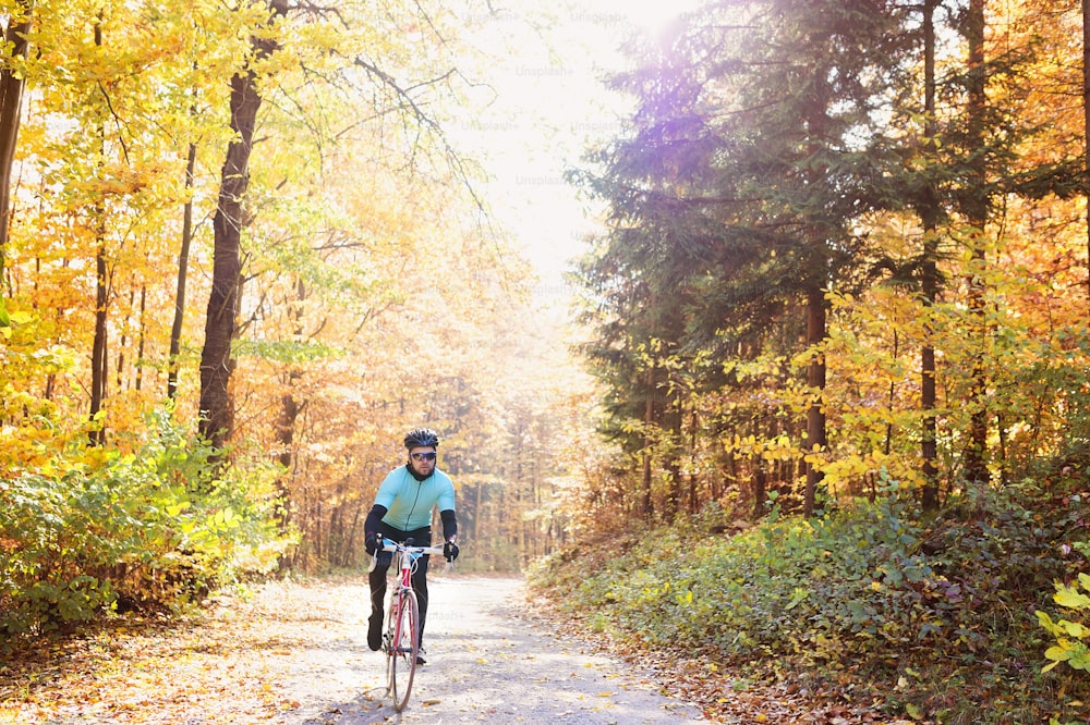 Joven deportista guapo montando su bicicleta al aire libre en la naturaleza soleada del otoño
