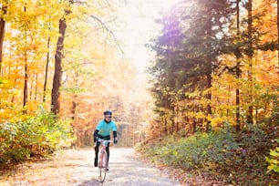 Jovem esportista bonito andando de bicicleta do lado de fora na natureza ensolarada do outono