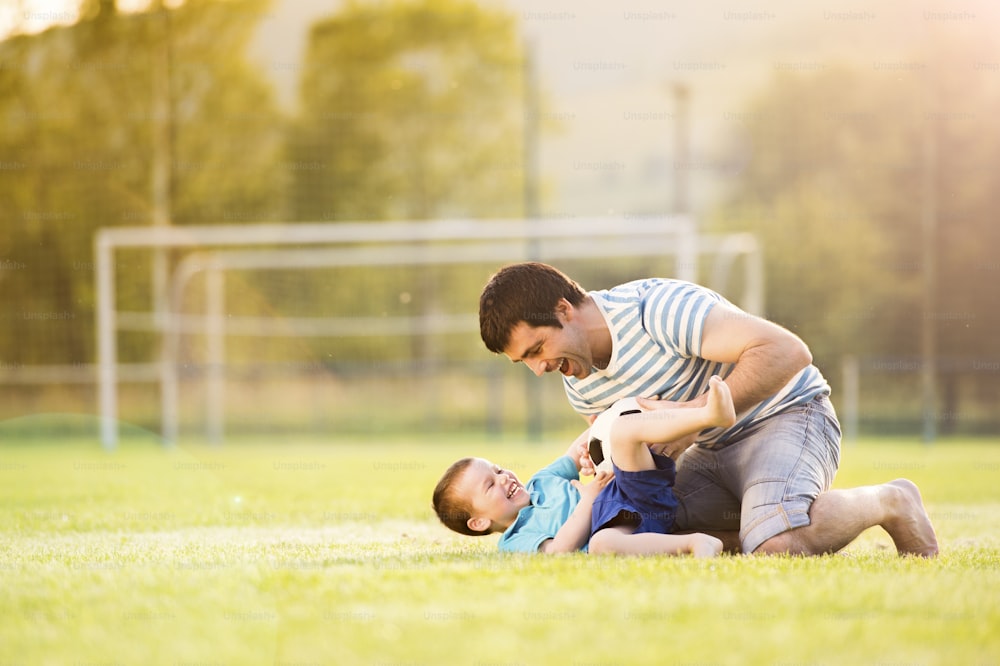 Padre joven con su hijo pequeño jugando al fútbol en el campo de fútbol