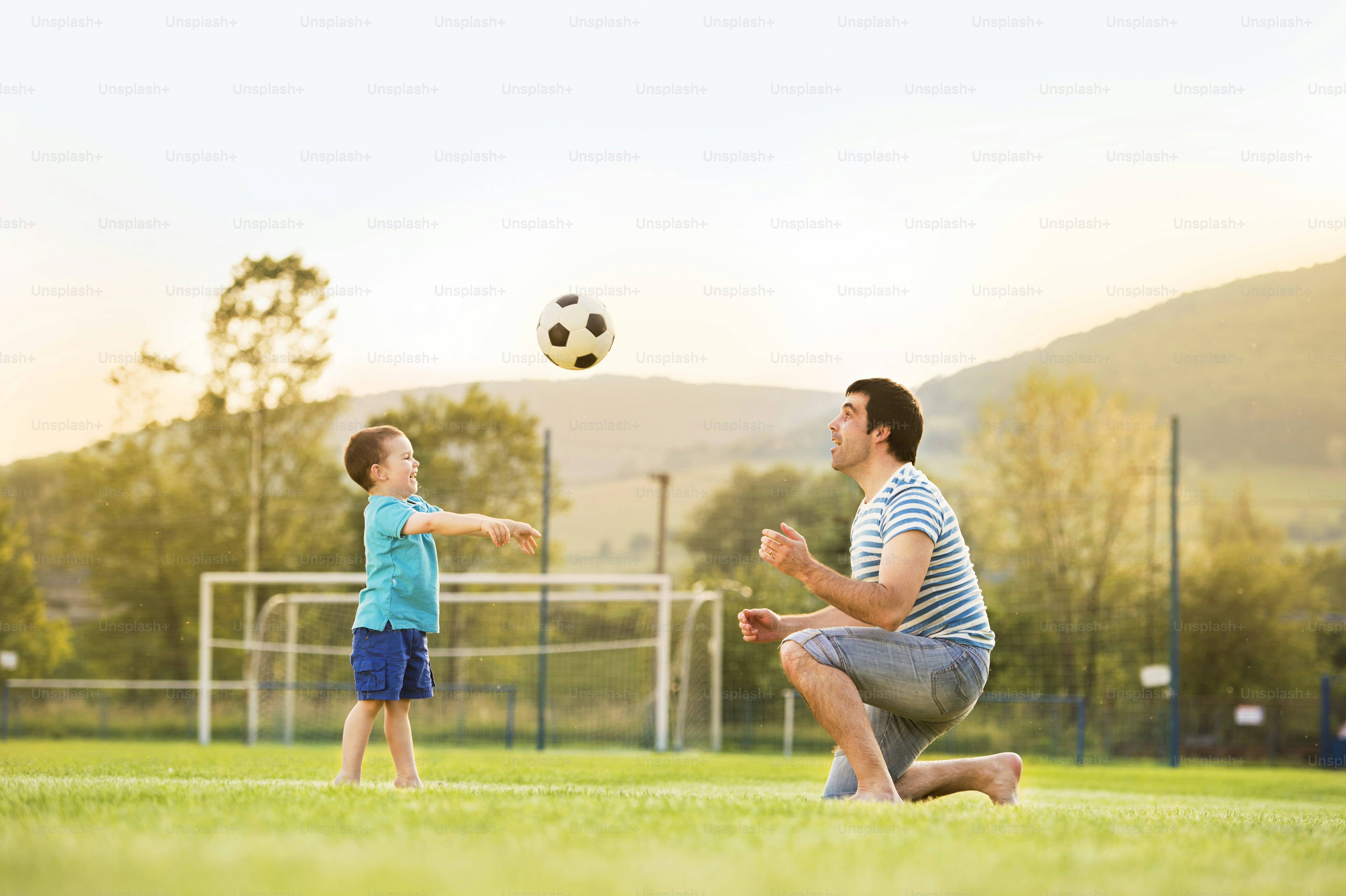 Young father with his little son playing football on football pitch