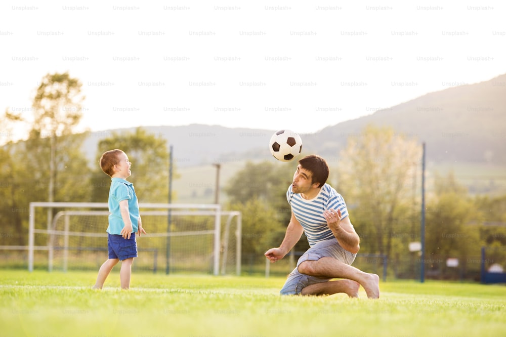 Jeune père avec son petit garçon jouant au football sur un terrain de football